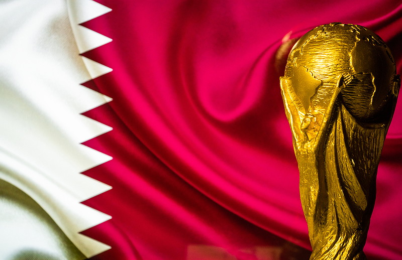 world cup trophy and qatar flag in the background